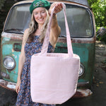 A woman holding the Daisy Embroidered Pastel Pink Linen Zipper Tote Bag showing off the back.