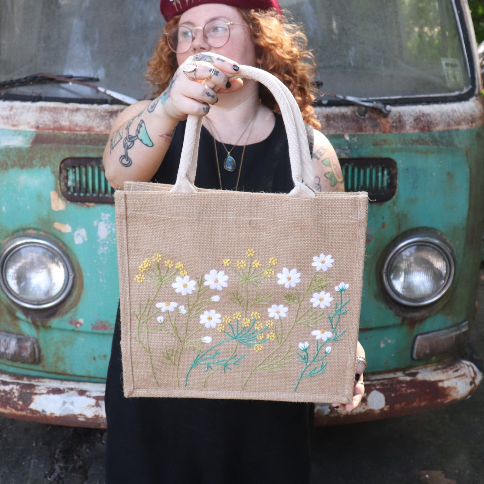 A woman wearing a black tank dress holding the Daisy Garden Embroidered Jute Bag.