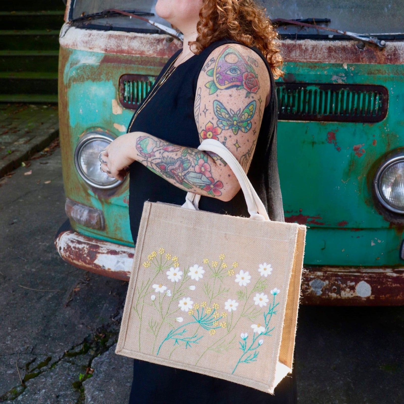 A woman wearing a black tank dress holding the Daisy Garden Embroidered Jute Bag.