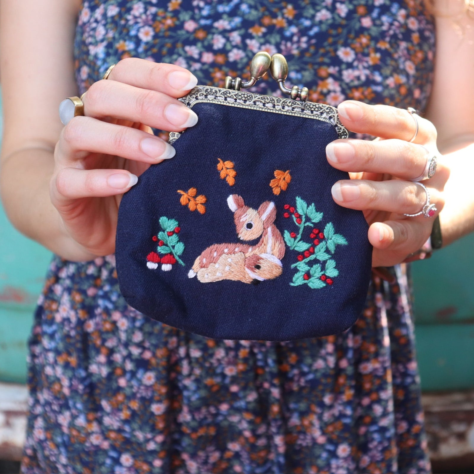 A woman in a navy floral dress holding the Deer Embroidered Navy Blue Coin Purse.