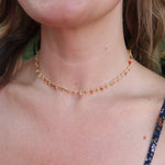 A woman wearing the orange Midsummer Gemstone Agate Gold Plated Necklace in front of some greenery.