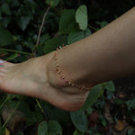 Someone wearing the orange agate Midsummer Gemstone Agate Gold Plated Anklet  in front of greenery.