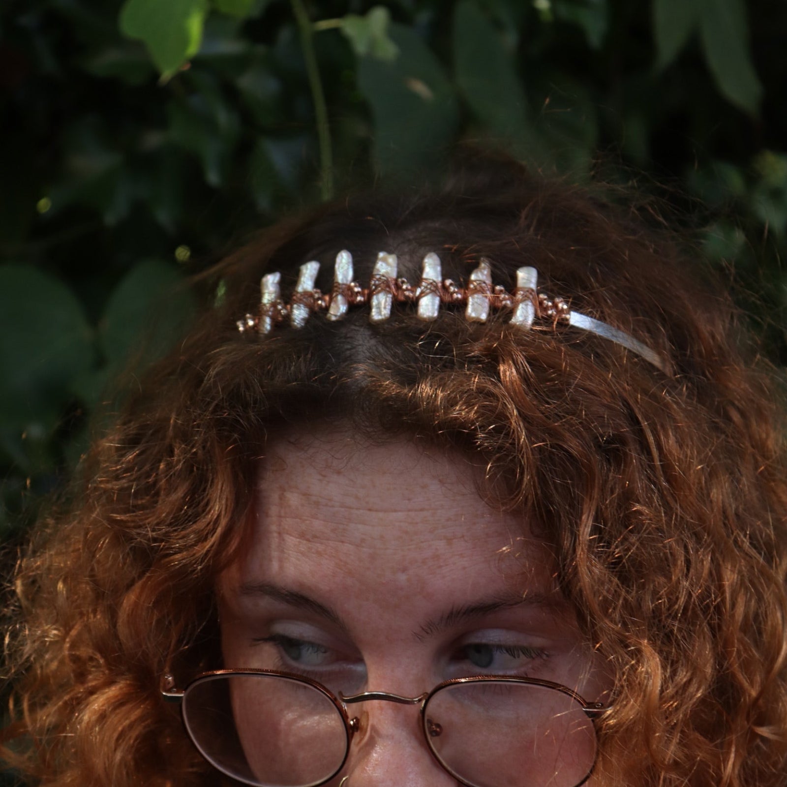 A red headed women wearing the Bridal Tiara - Rose Gold Hematite & Freshwater Pearl in front of greenery.