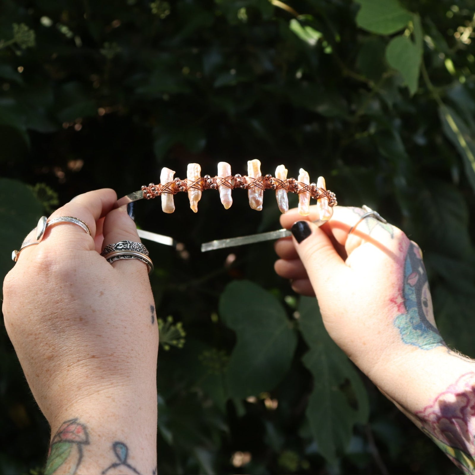 Someone holding the Bridal Tiara - Rose Gold Hematite & Freshwater Pearl in front of greenery.