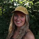 A woman wearing the Daisy Garden Embroidered Adjustable Baseball Cap with a navy floral dress in front of greenery.