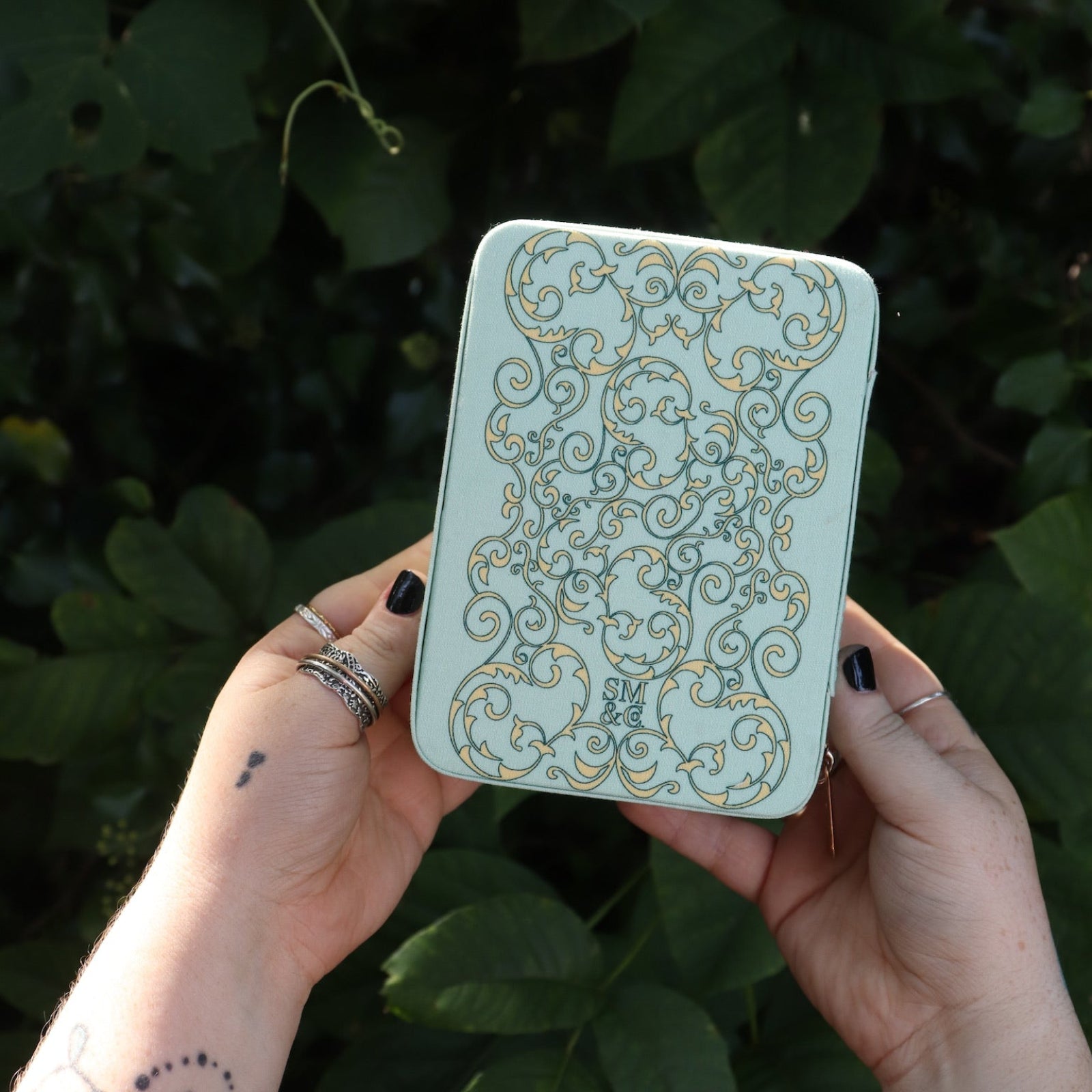 Someone holding the Once Upon a Time Travel Jewelry Organizer in front of greenery, showing off the back.