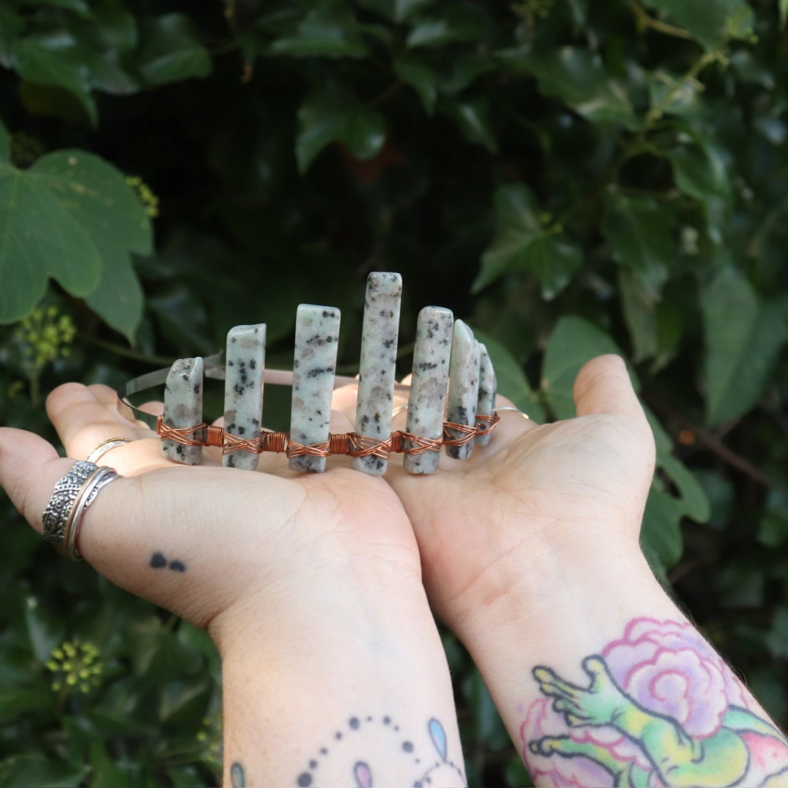A woman holding the Gemstone Tiara / Crown - Kiwi Jasper - Sesame in front of greenery.