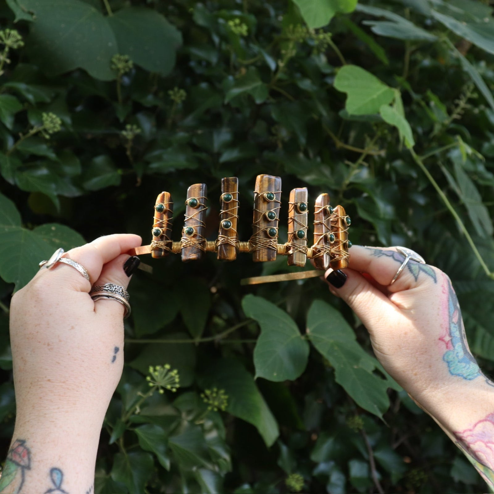 Someone holding the Tigers Eye & Malachite Tiara in front of greenery.