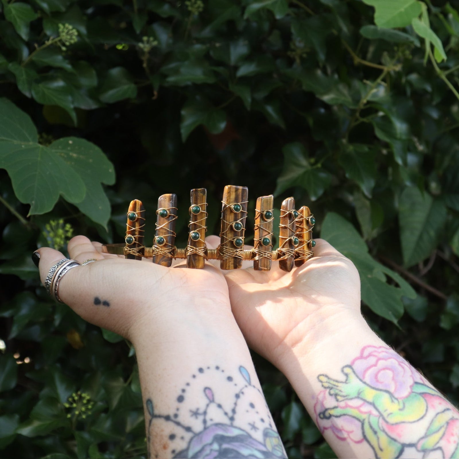 Someone holding the Tigers Eye & Malachite Tiara in front of greenery.