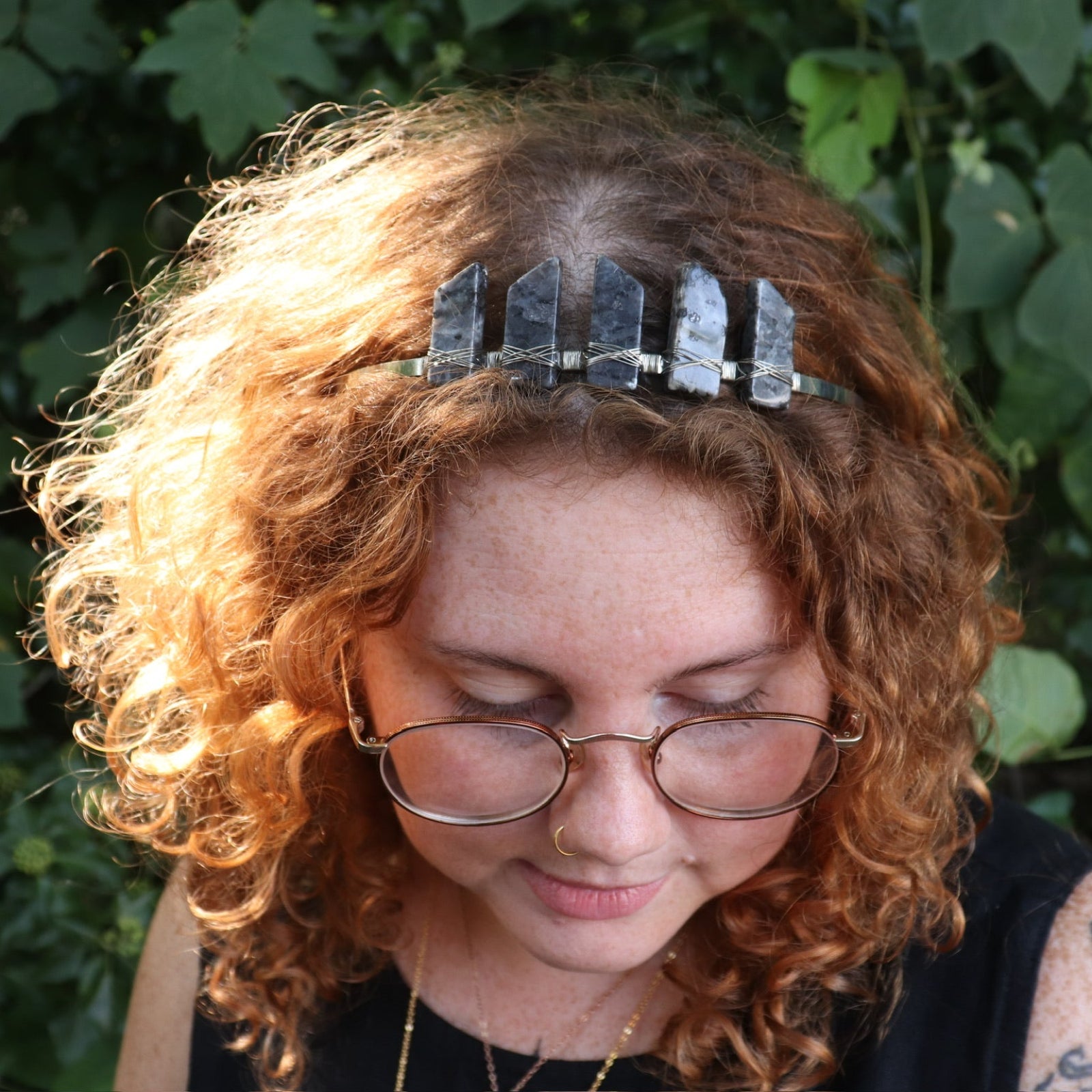 A woman wearing the Fairy Crown / Celtic Tiara - Black Labradorite / Larvikite in front of greenery.