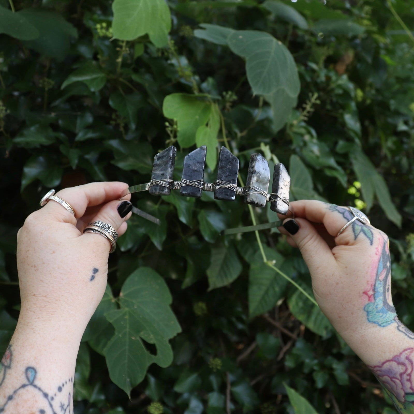 Someone holding the Fairy Crown / Celtic Tiara - Black Labradorite / Larvikite in front of greenery.