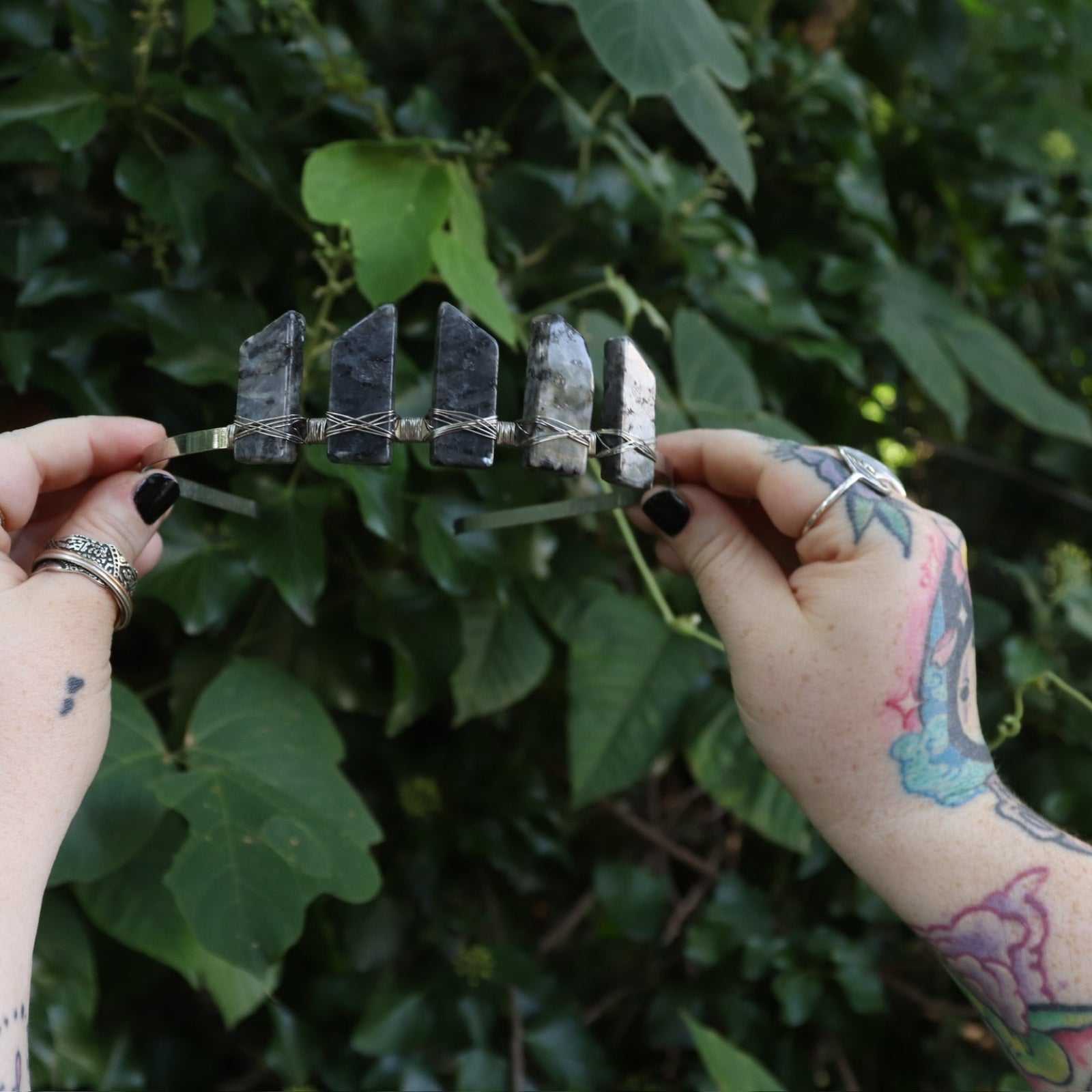 Someone holding the Fairy Crown / Celtic Tiara - Black Labradorite / Larvikite in front of greenery.