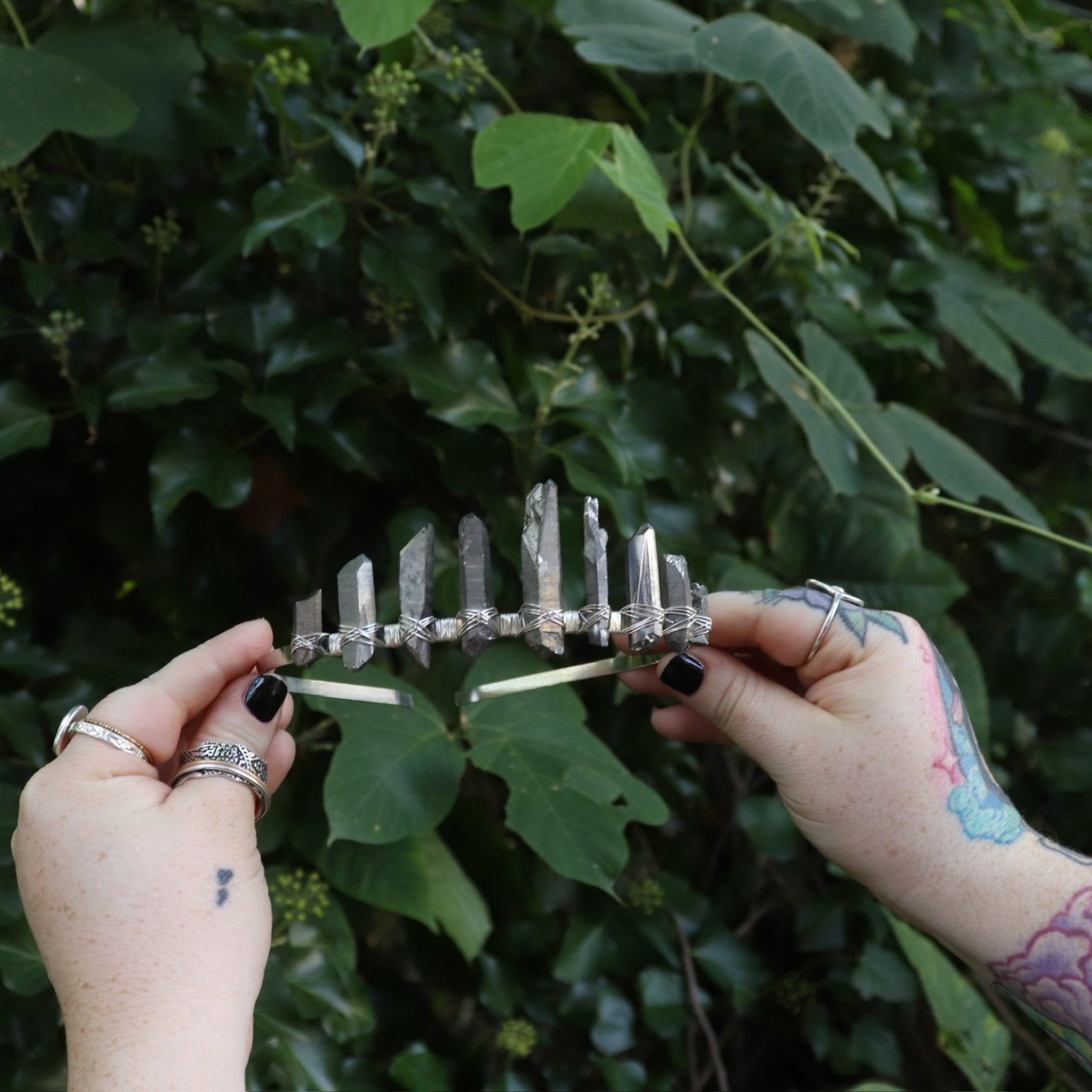 Someone holding the Fairy Crown / Celtic Tiara - Titanium Quartz in front of greenery.