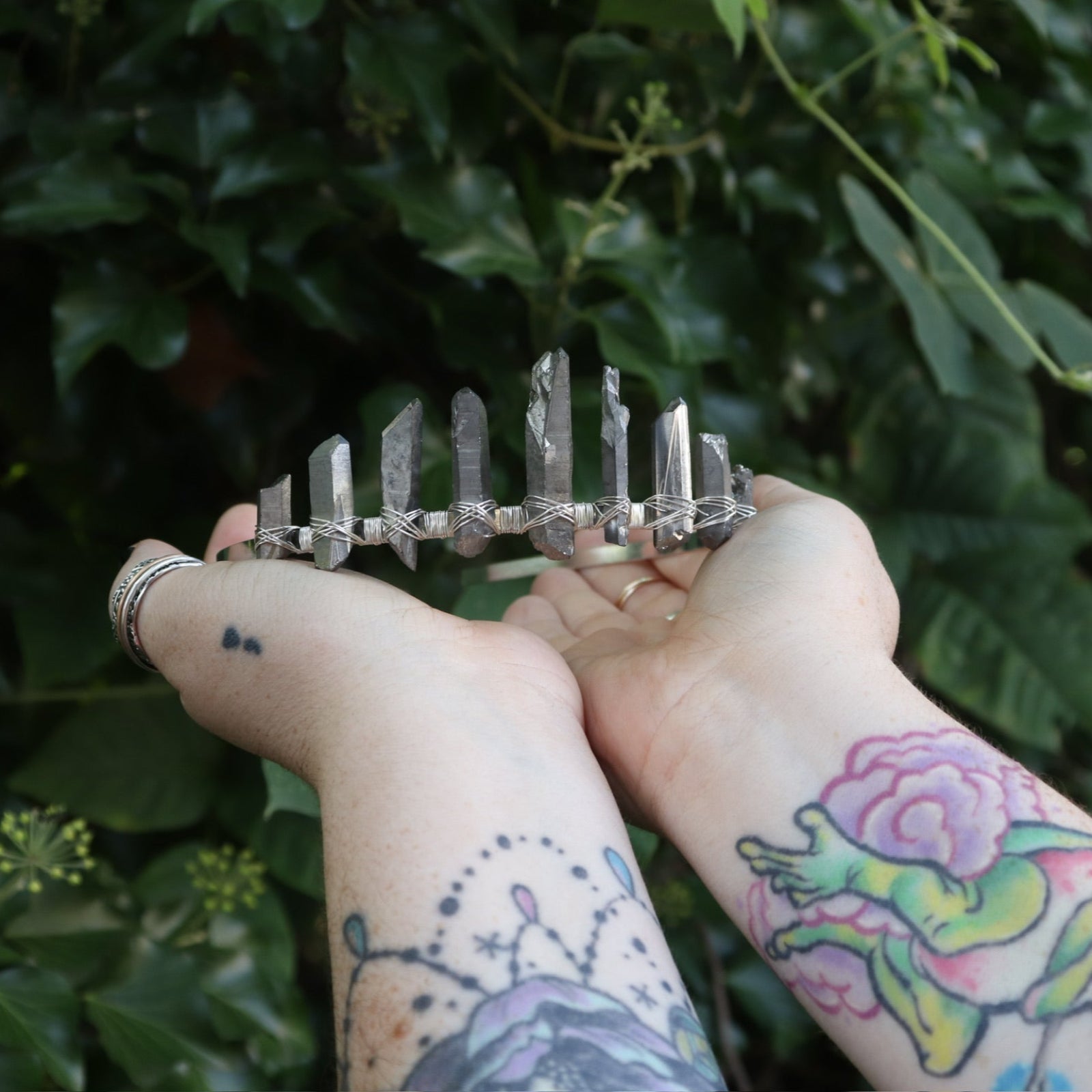 Someone holding the Fairy Crown / Celtic Tiara - Titanium Quartz in front of greenery.