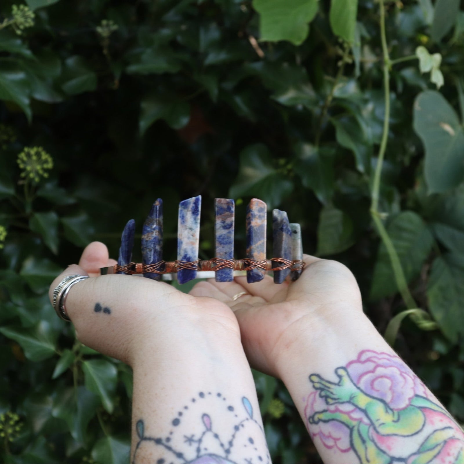 Someone holding the Fairy Crown / Celtic Tiara - Orange & Blue Sodalite in front of greenery.