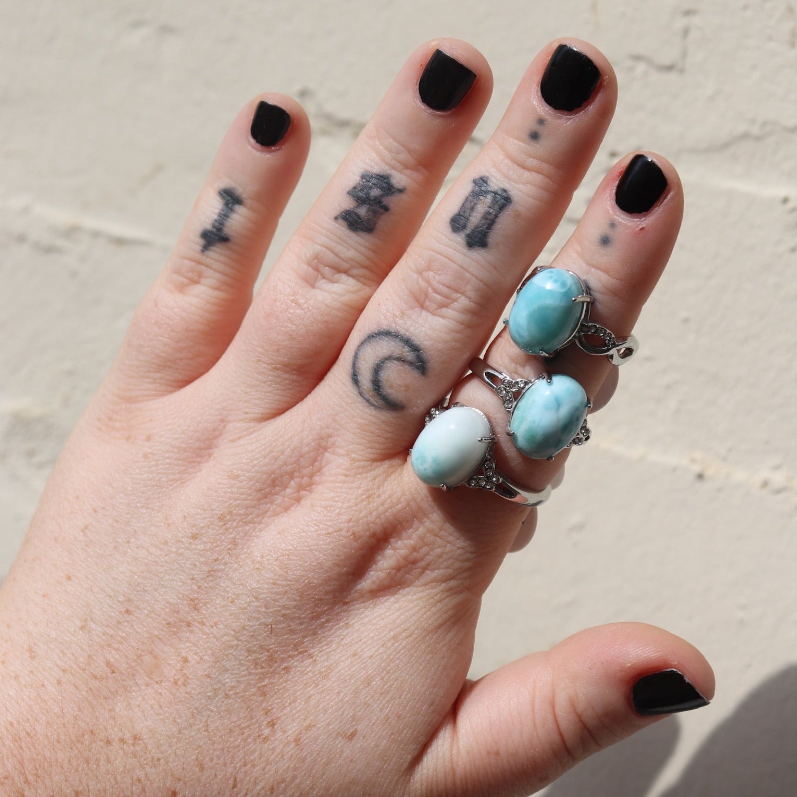 Someone wearing three of the Natural Larimar Stainless Steel Rings in front of a white wall.