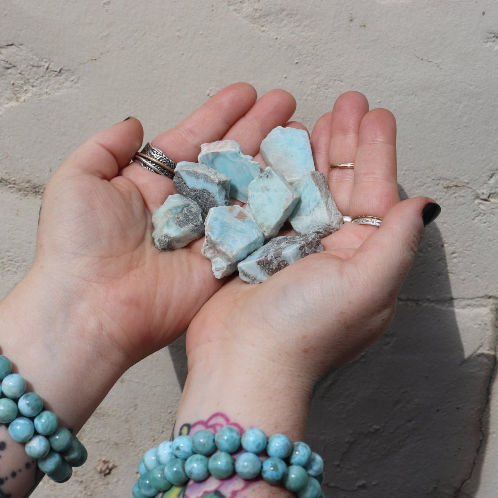 Someone holding multiple Natural Larimar Small Crystal Slabs in front of a white wall.