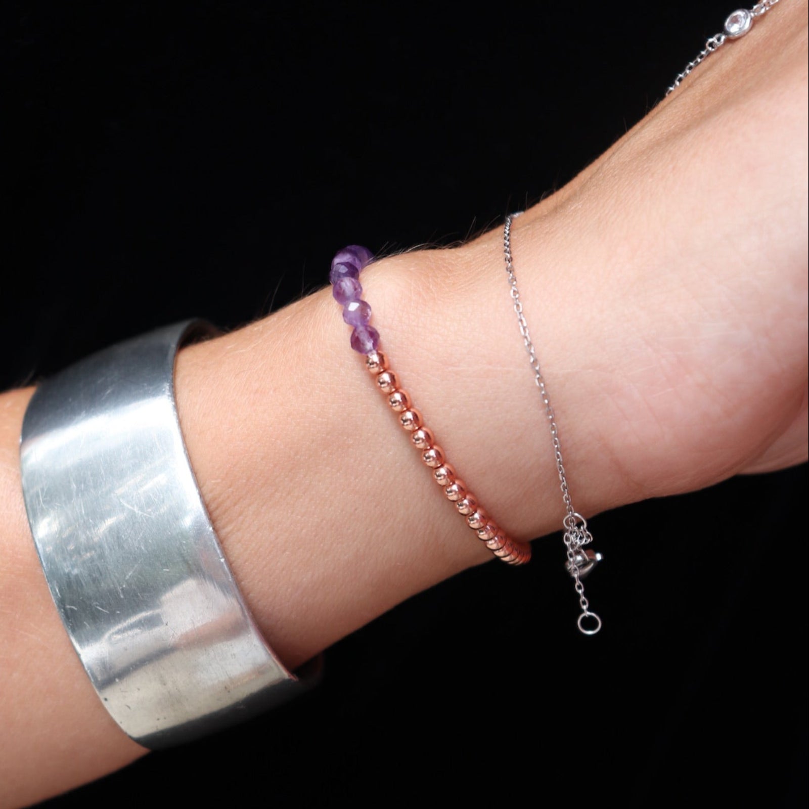 Someone wearing the Dainty Multi-Faceted Amethyst beads + Copper Bracelet in front of a black background.