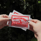 Someone holding three of the Fortune Fish packages in front of the greenery.