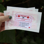 Someone holding three of the Fortune Fish packages in front of the greenery, showing off the back.