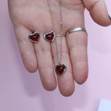 Someone holding the silver Carnelian Earrings & Necklace Gift Jewelry Set in front of a pink background.