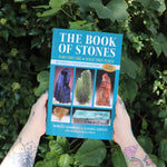 Someone holding the Book of Stones by Robert Simmons in front of greenery.
