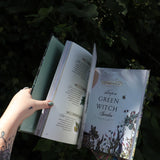 Someone holding the Green Witch Illustrated by Arin Murphy-Hiscock open in front of the greenery, showing off the pages.