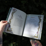 Someone holding the Green Witch Illustrated by Arin Murphy-Hiscock open in front of the greenery, showing off the pages.