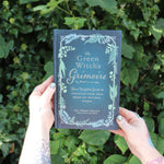 Someone holding the Green Witch's Grimoire by Arin Murphy-Hiscock in front of greenery.