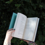 Someone holding the Green Witch's Grimoire by Arin Murphy-Hiscock open in front of greenery, showing off the pages.