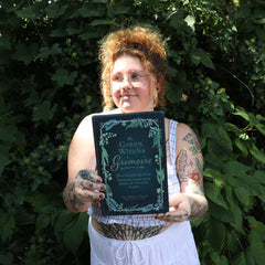 A woman holding the Green Witch's Grimoire by Arin Murphy-Hiscock in front of greenery.
