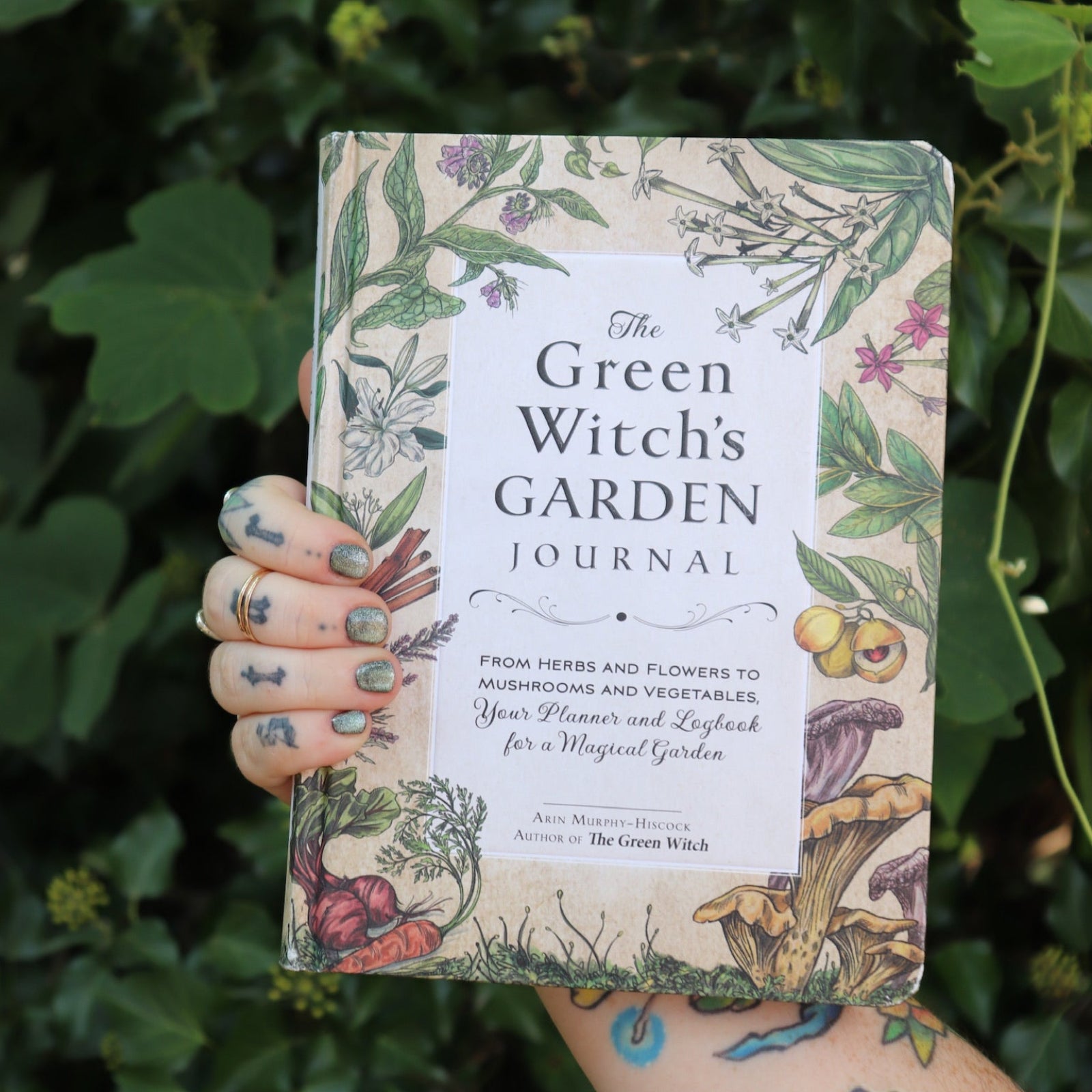 Someone holding the Green Witch's Garden Journal by Arin Murphy-Hiscock in front of greenery.