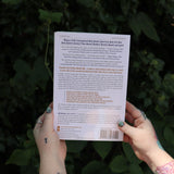 Someone holding the Ultimate College Student Health Handbook by Jill Grimes in front of greenery, showing off the back.