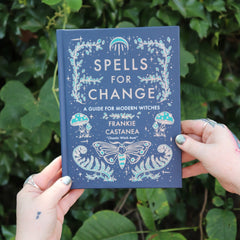 Someone holding the Spells for Change Hardcover Book in front of greenery.