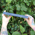 Someone holding the Spells for Change Hardcover Book in front of greenery, showing off the side.