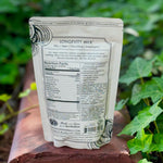 The back of the 7 Mushrooms Mocha Milk - Longevity Milk on a dusty red surface surrounded by ivy.