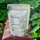 The back of the 7 Mushrooms Mocha Milk - Longevity Milk on a dusty red surface surrounded by ivy.