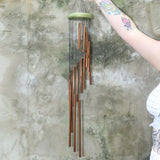 Someone holding the Green Woodstock Habitats™ Rainfall Wind Chime up in front of a concrete wall.