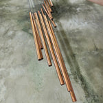 An up close image of someone holding the Green Woodstock Habitats™ Rainfall Wind Chime up in front of a concrete wall.