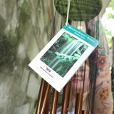 An up close image of someone holding the Green Woodstock Habitats™ Rainfall Wind Chime up in front of a concrete wall.