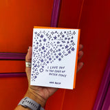 Someone holding the Outer Space I Love You Letterpress Greeting Card in front of an orange and pink wall.
