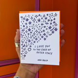 Someone holding the Outer Space I Love You Letterpress Greeting Card in front of an orange and pink wall.