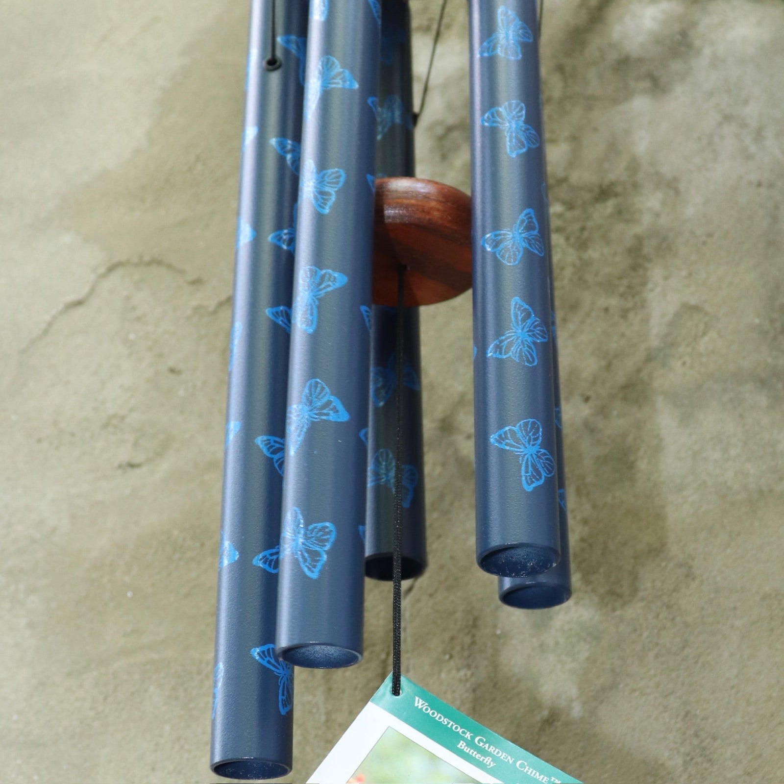 An up close image of someone holding the Butterfly Woodstock Garden Chime™ in front of a concrete wall.