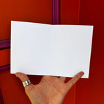 Someone holding the Outer Space I Love You Letterpress Greeting Card in front of an orange and pink wall.