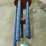 An up close image of someone holding the Butterfly Woodstock Garden Chime™ in front of a concrete wall.