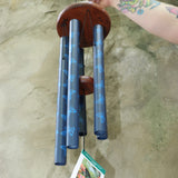 An up close image of someone holding the Butterfly Woodstock Garden Chime™ in front of a concrete wall.