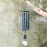Someone holding the Chimes of Provence™ - Navy Wind Chime in front of a concrete wall.