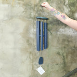 Someone holding the Chimes of Provence™ - Navy Wind Chime in front of a concrete wall.