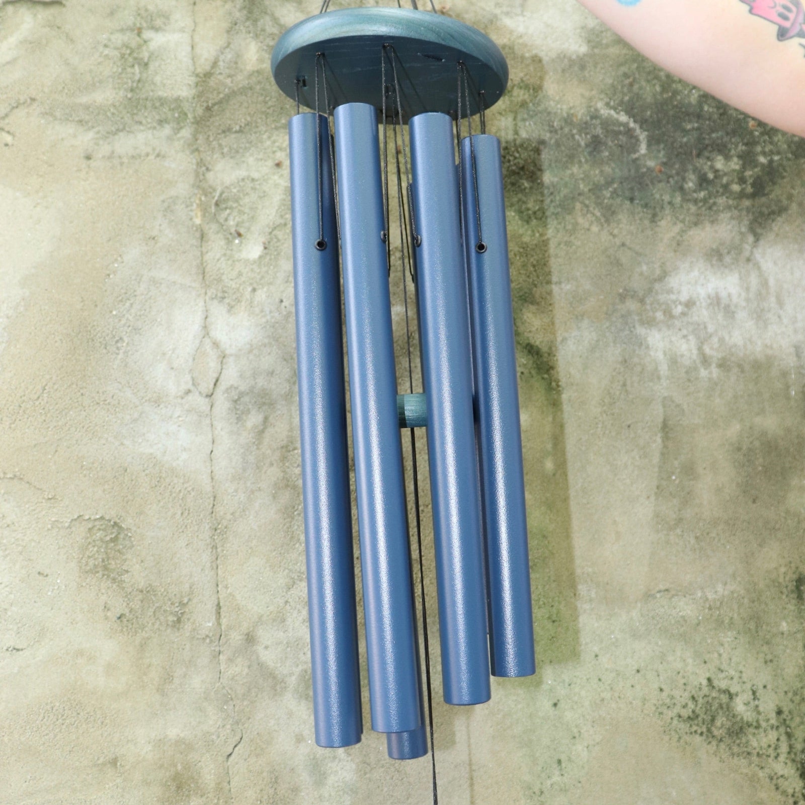 An up-close image of someone holding the Chimes of Provence™ - Navy Wind Chime in front of a concrete wall.