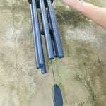 An up-close image of someone holding the Chimes of Provence™ - Navy Wind Chime in front of a concrete wall.